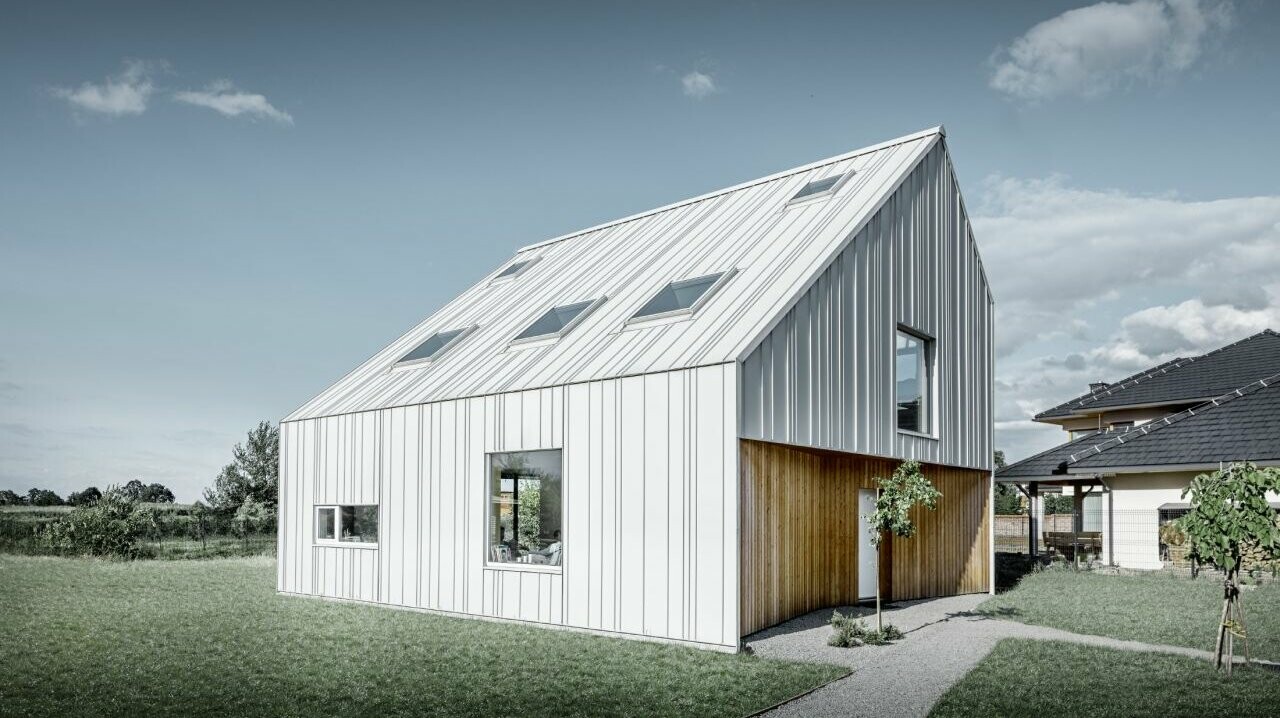 Modern detached house with gable roof, the entire outer skin is clad with PREFALZ in PREFA white. The panels of different widths extend from the roof over the façade. Several roof windows are installed in the roof.