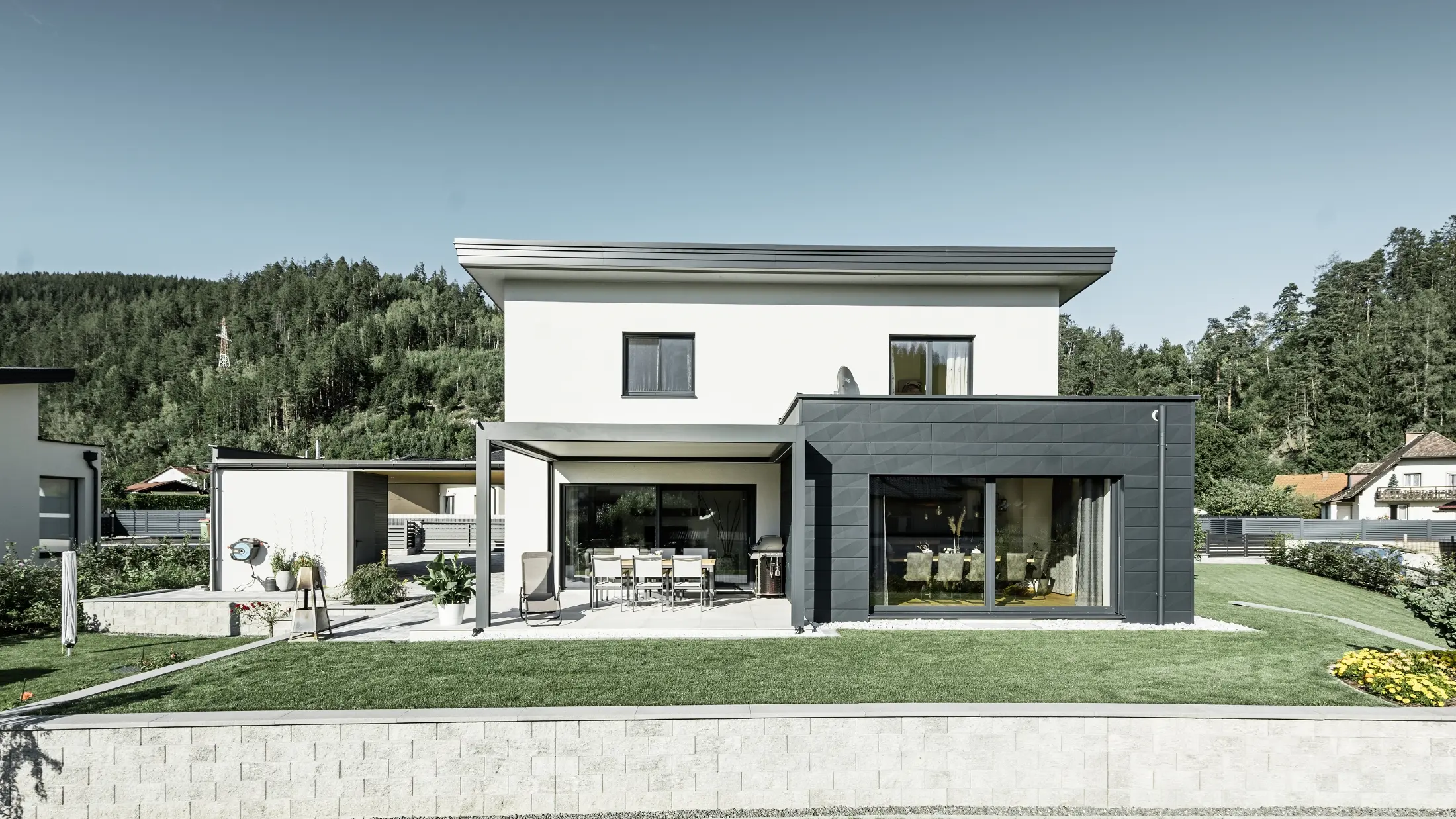 Neu gebautes Einfamilienhaus mit Zubau; Anbau hebt sich optisch vom Rest des Hauses ab, da er mit dem PREFA Fassadenpaneelen Siding.X in Anthrazit verkleidet ist. Der Rest der Fassade ist weiß verputzt.
