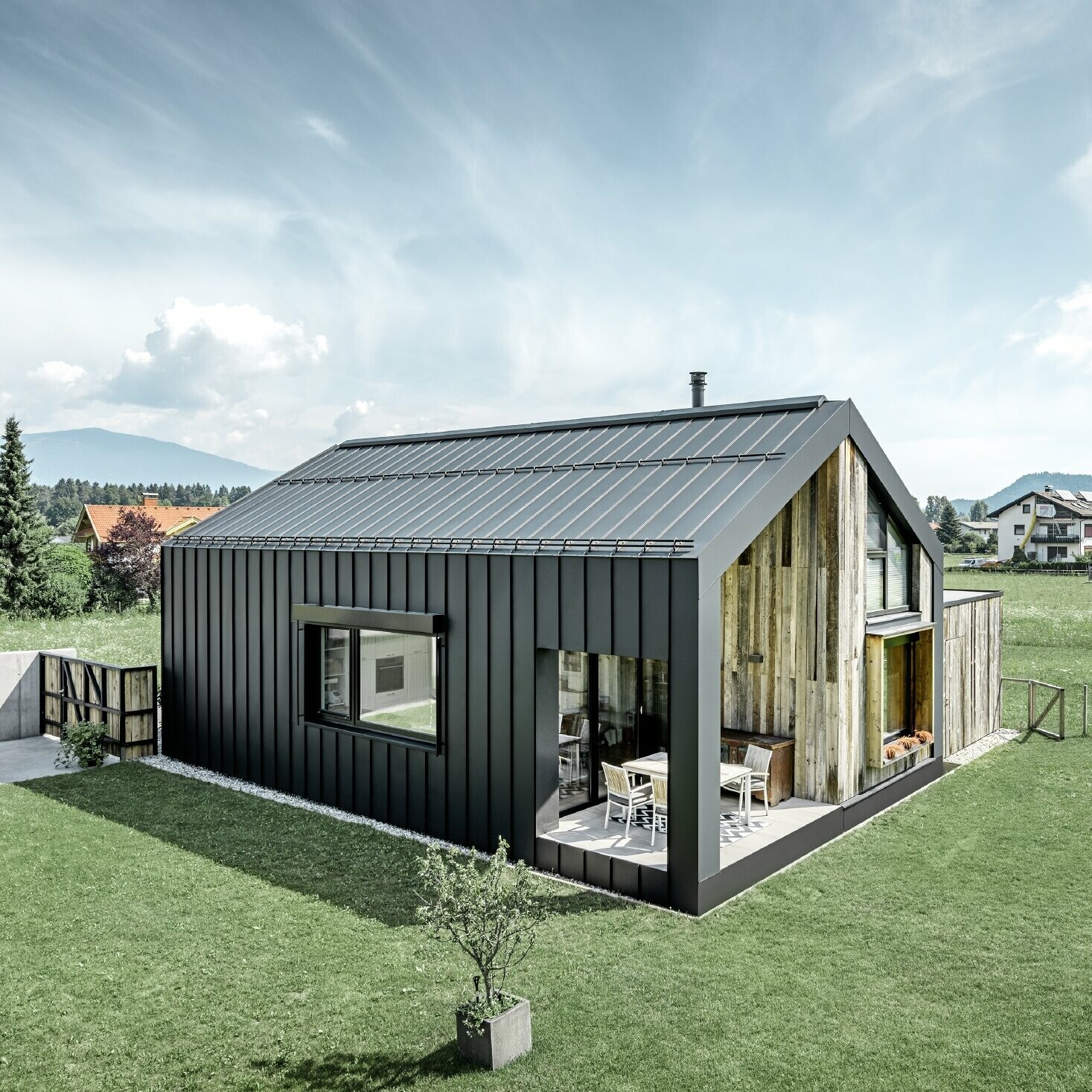 Detached house with gable roof, roof and façade are covered with PREFALZ from PREFA in P.10 anthracite. The panels of the roof surface extend across the façade. Part of the façade is clad with weathered wood.