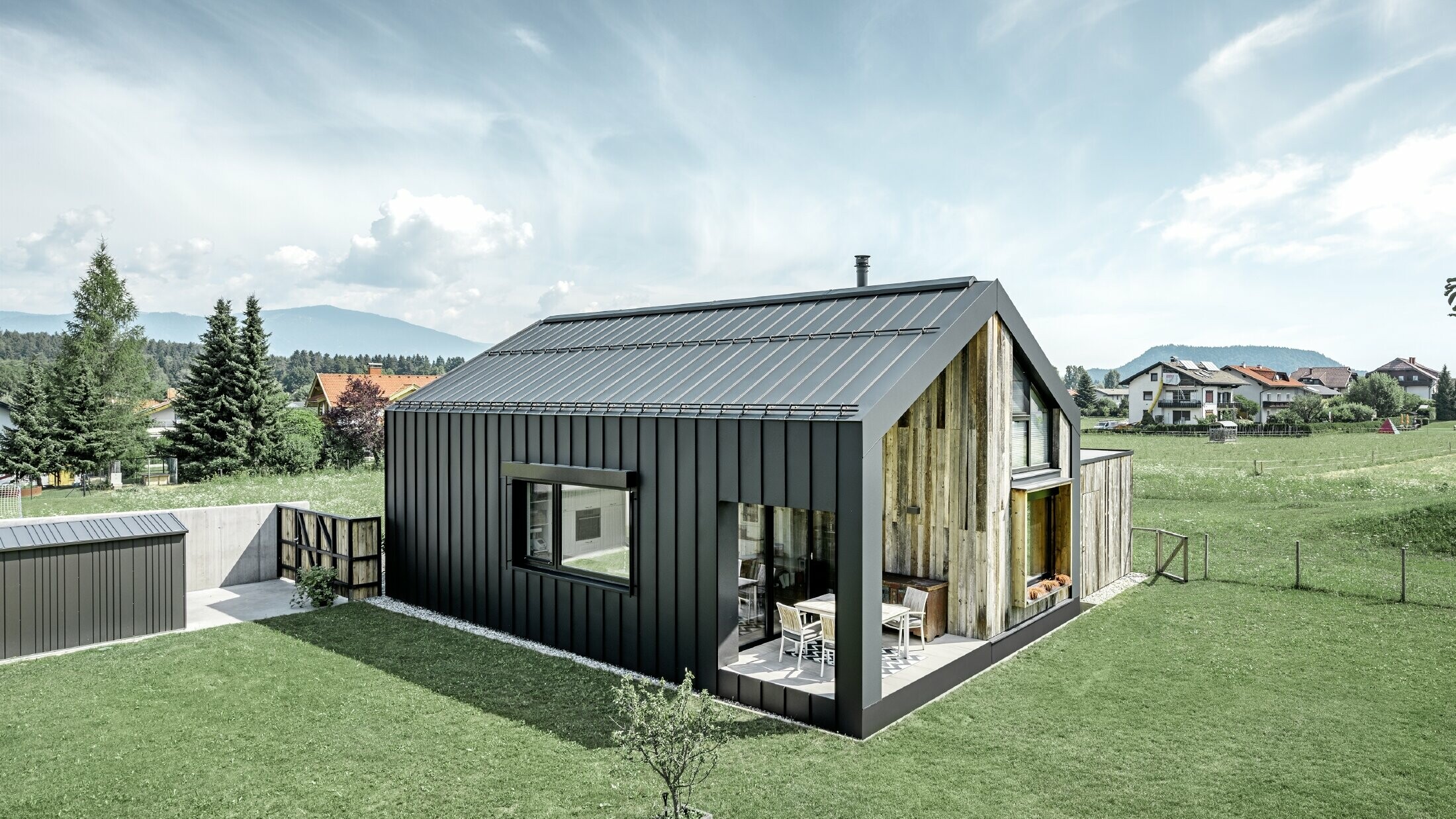 Detached house with gable roof, roof and façade are covered with PREFALZ from PREFA in P.10 anthracite. The panels of the roof surface extend across the façade. Part of the façade is clad with weathered wood.