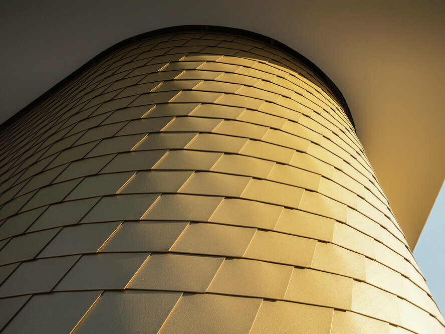 Detailed view of a curved wall cladding with the PREFA façade shingle in maya gold