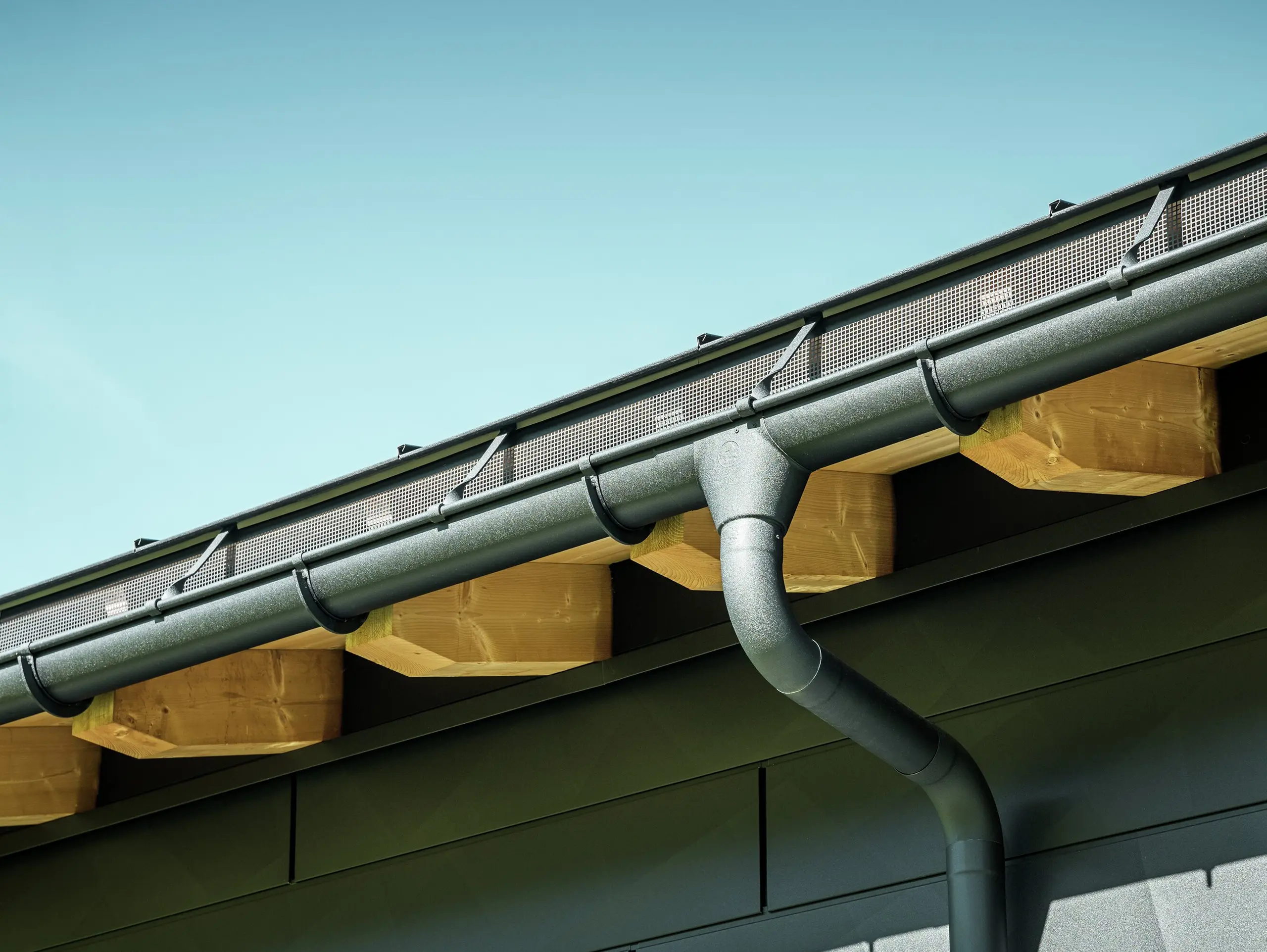 Close-up of the façade of a modern detached house in Ascharina, Switzerland. The sides of the building were clad with striking PREFA Siding.X façade panels in P.10 black. The PREFA roof drainage system with half-round gutter and downpipe is colour-coordinated.