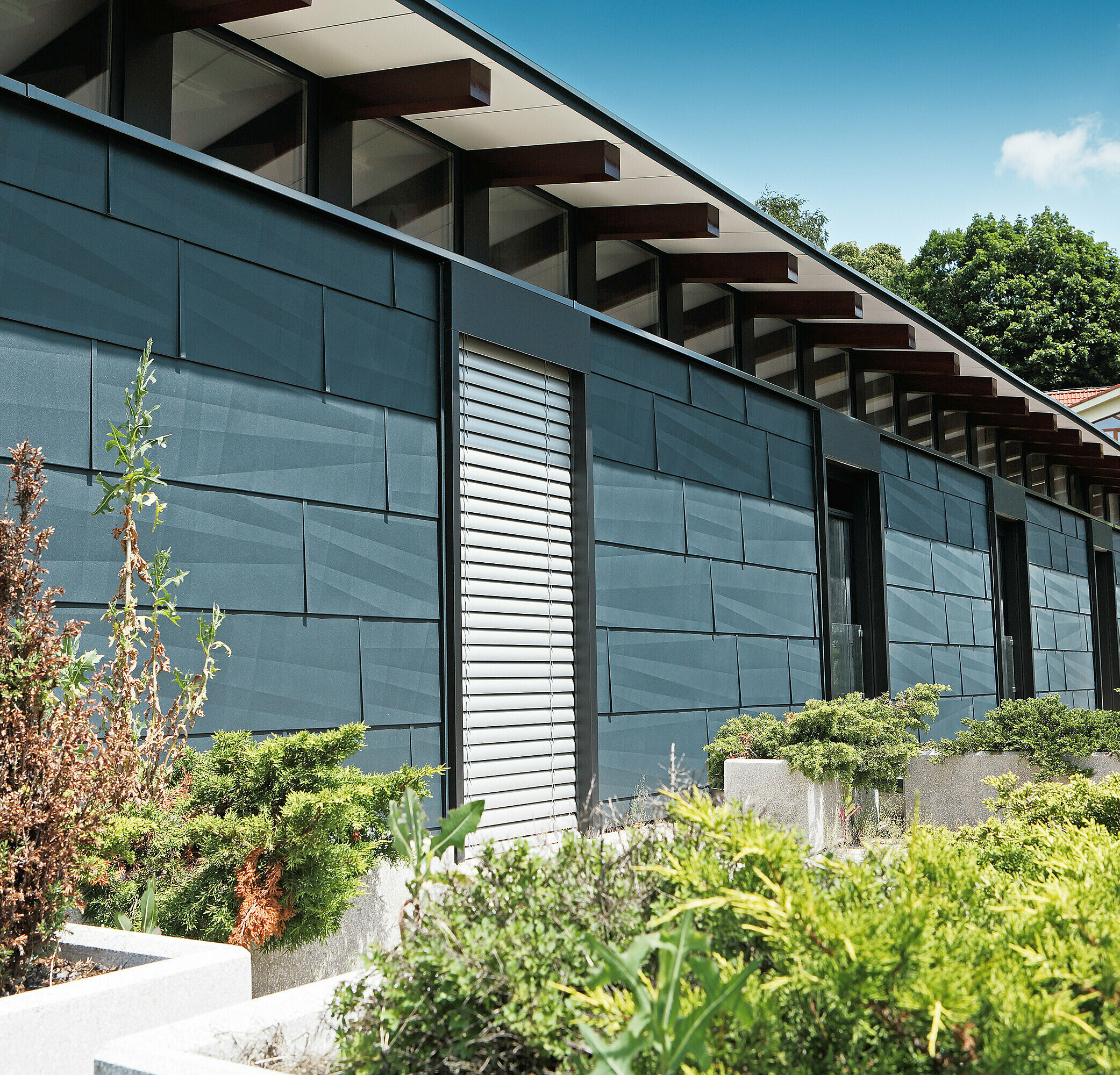 Modern exposed building side designed using FX.12 façade panelling in anthracite, with a garden.