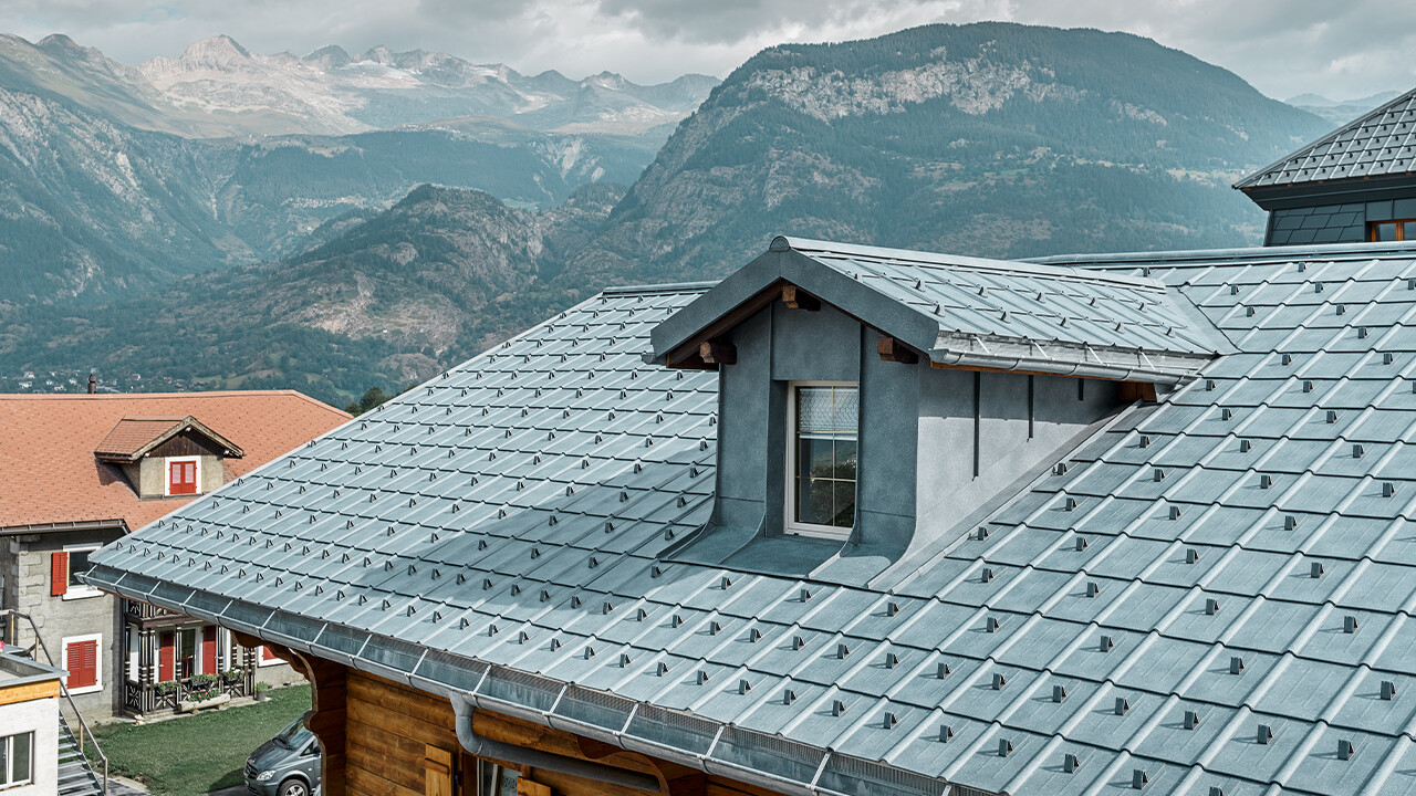 Gabled roof with dormers. A PREFA sheet metal roof is installed on the roof area with the roof tiles in stone grey. The dormer is clad in a PREFA angular standing seam in stone grey.