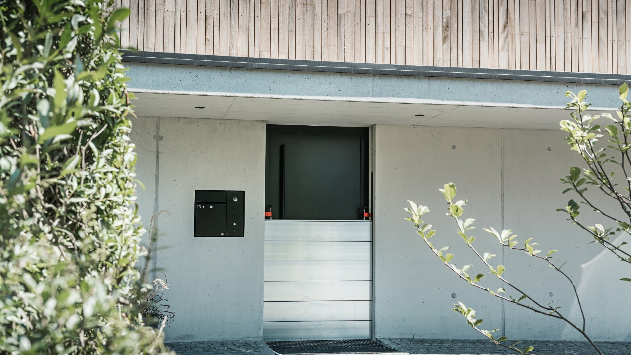 PREFA flood protection is installed in front of the entrance door of a detached house with a wooden façade. 