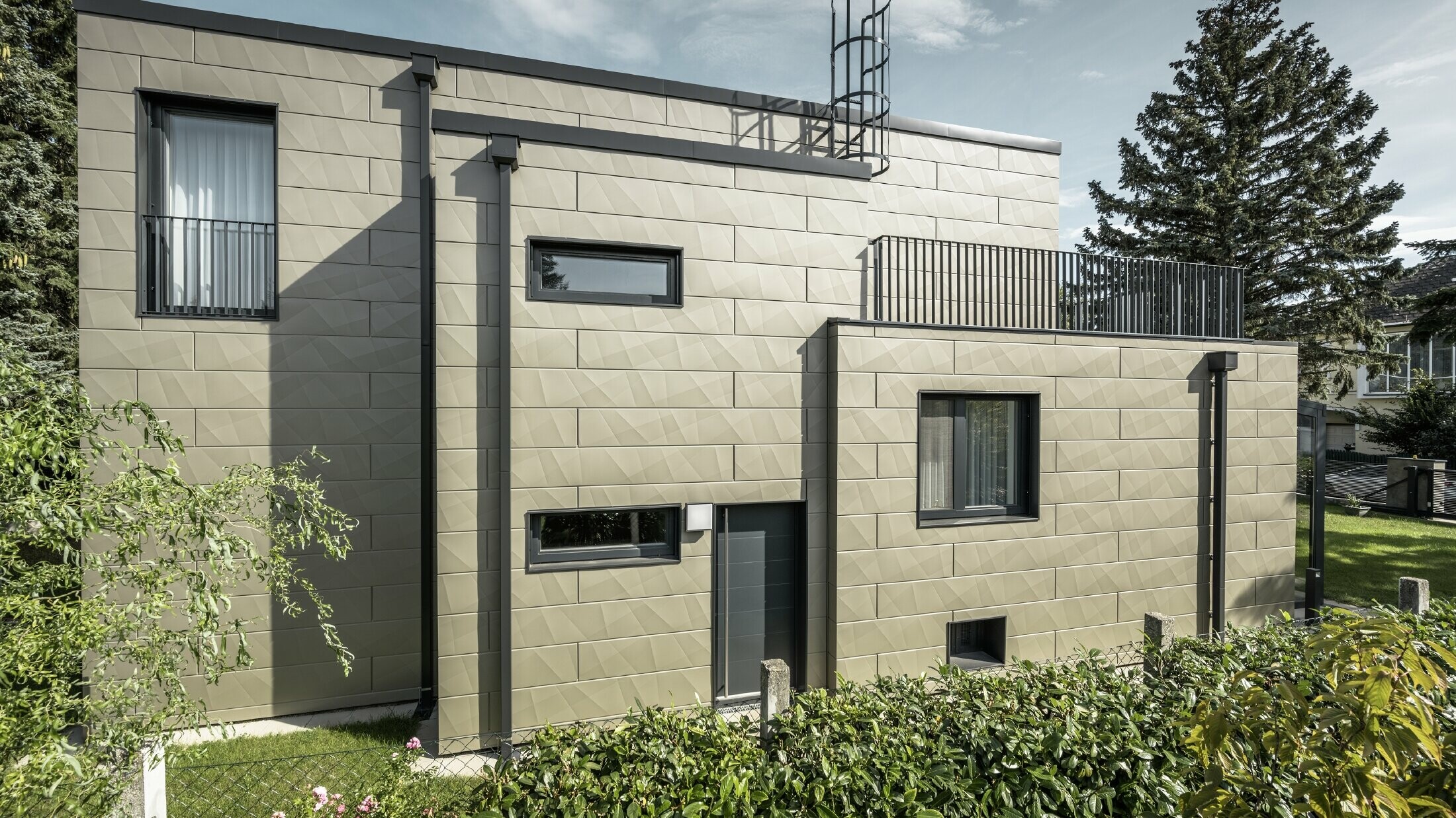 New building with a flat roof, the façade is clad with the PREFA Siding.X façade panel with edges in bronze, the flashings, as well as the square downpipe, and the PREFA square downpipe are made of anthracite.   