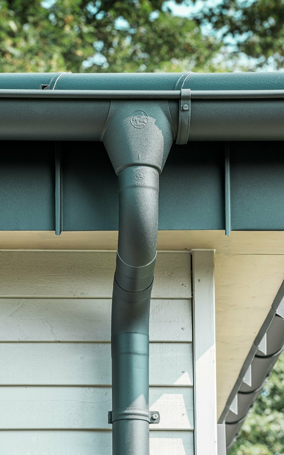 Nahaufnahme der robusten PREFA Dachentwässerung eines Bungalows in Rommerskirchen. Die hochwertige Saumrinne und das Ablaufrohr in P.10 Schwarz bieten optimalen Schutz vor Witterungseinflüssen. Langlebigkeit und Funktionalität verbinden sich hier mit elegantem Design aus Aluminium.