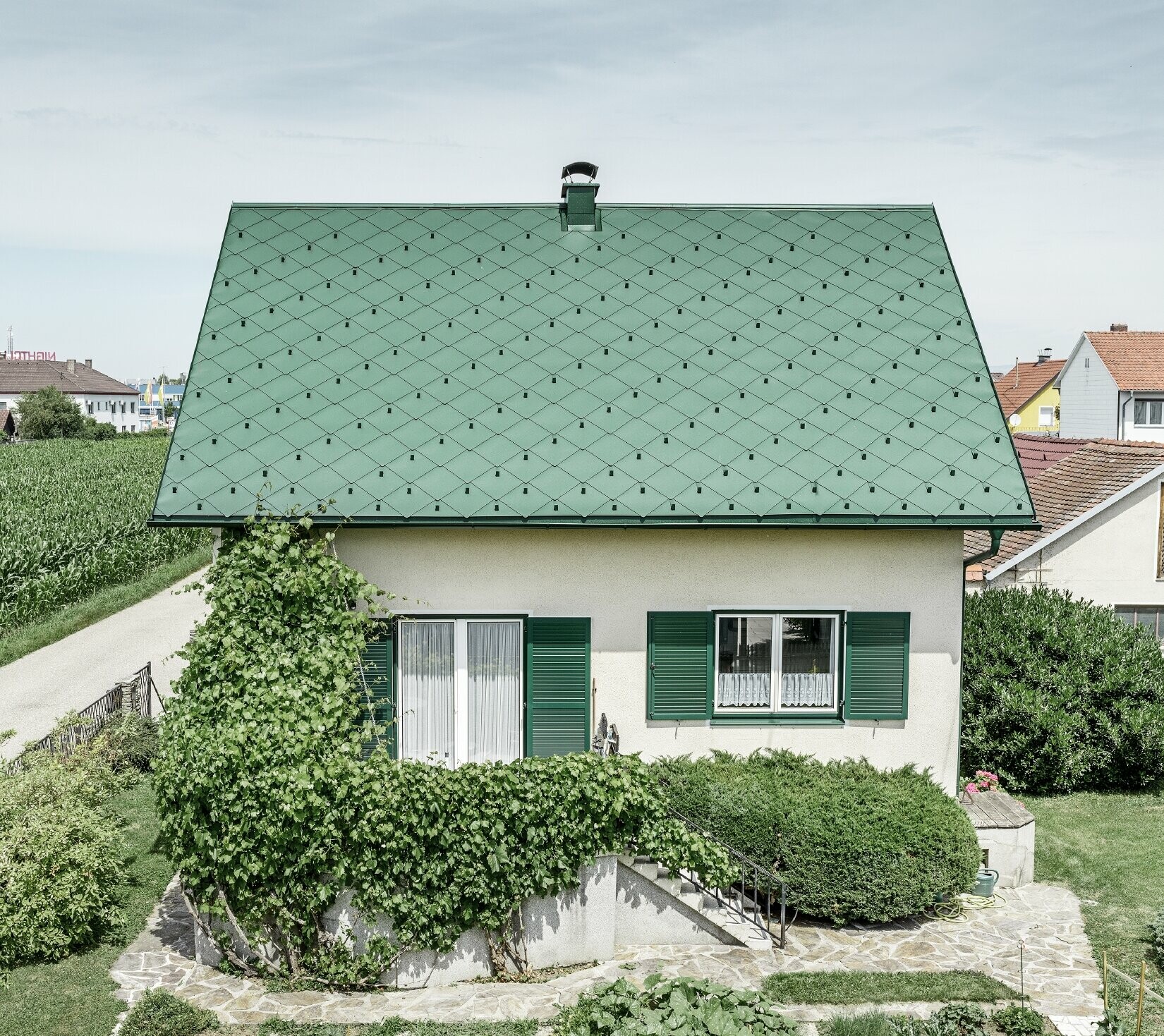 Classic detached house with a gable roof with an aluminium roof covering in moss green with green shutters. The roof was covered with PREFA rhomboid roof tiles 44 × 44 in P.10 moss green.