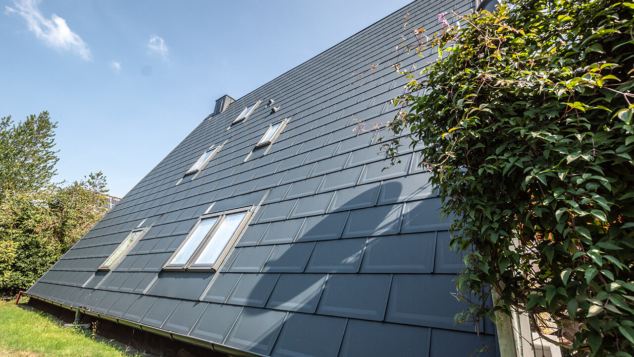 The long roof area of an A-frame house covered with the PREFA roof tile in P.10 anthracite. A number of roof-top windows are integrated into the roof area.