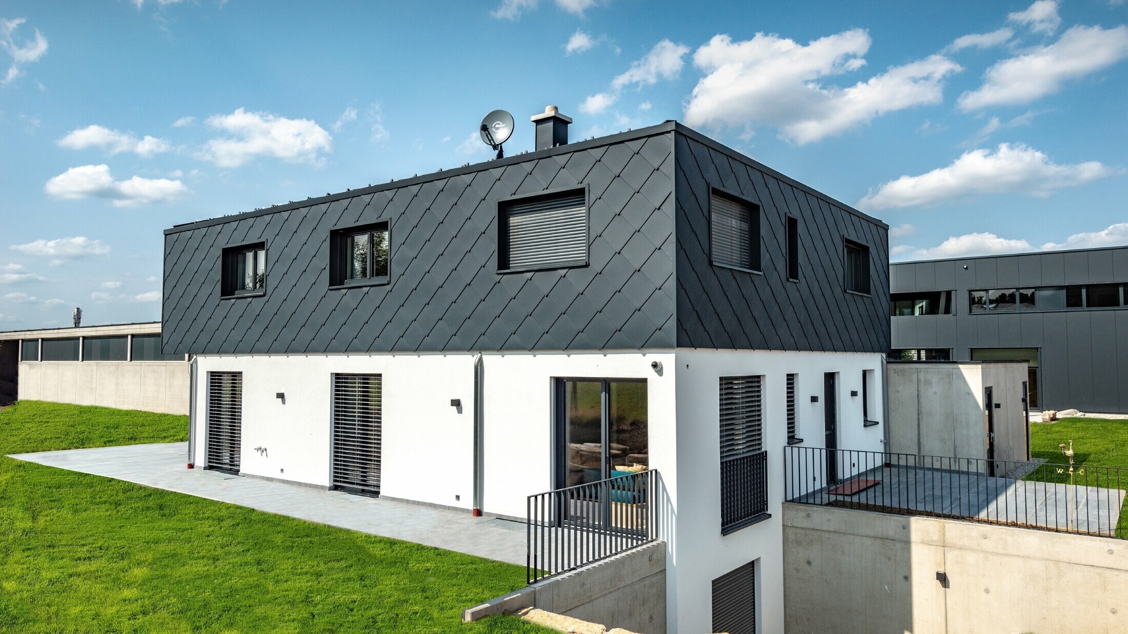 Modest new build with flat roof; the ground floor has a white plaster finish while the upper floor is clad in the large PREFA rhomboid façade tile in anthracite.