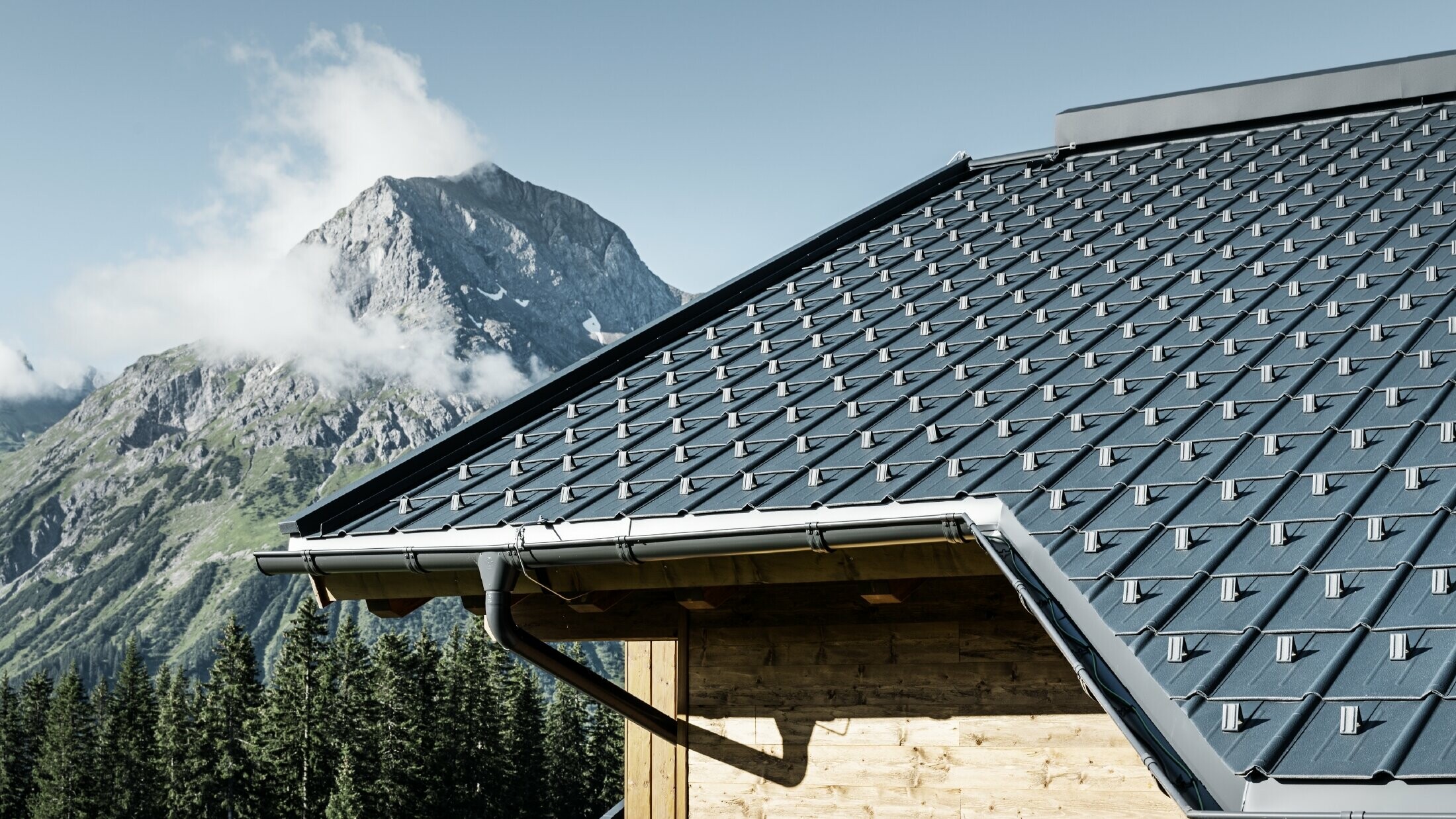 Wooden house in the mountains, the roof is covered with PREFA roof tiles in anthracite with a PREFA gutter and wooden façade