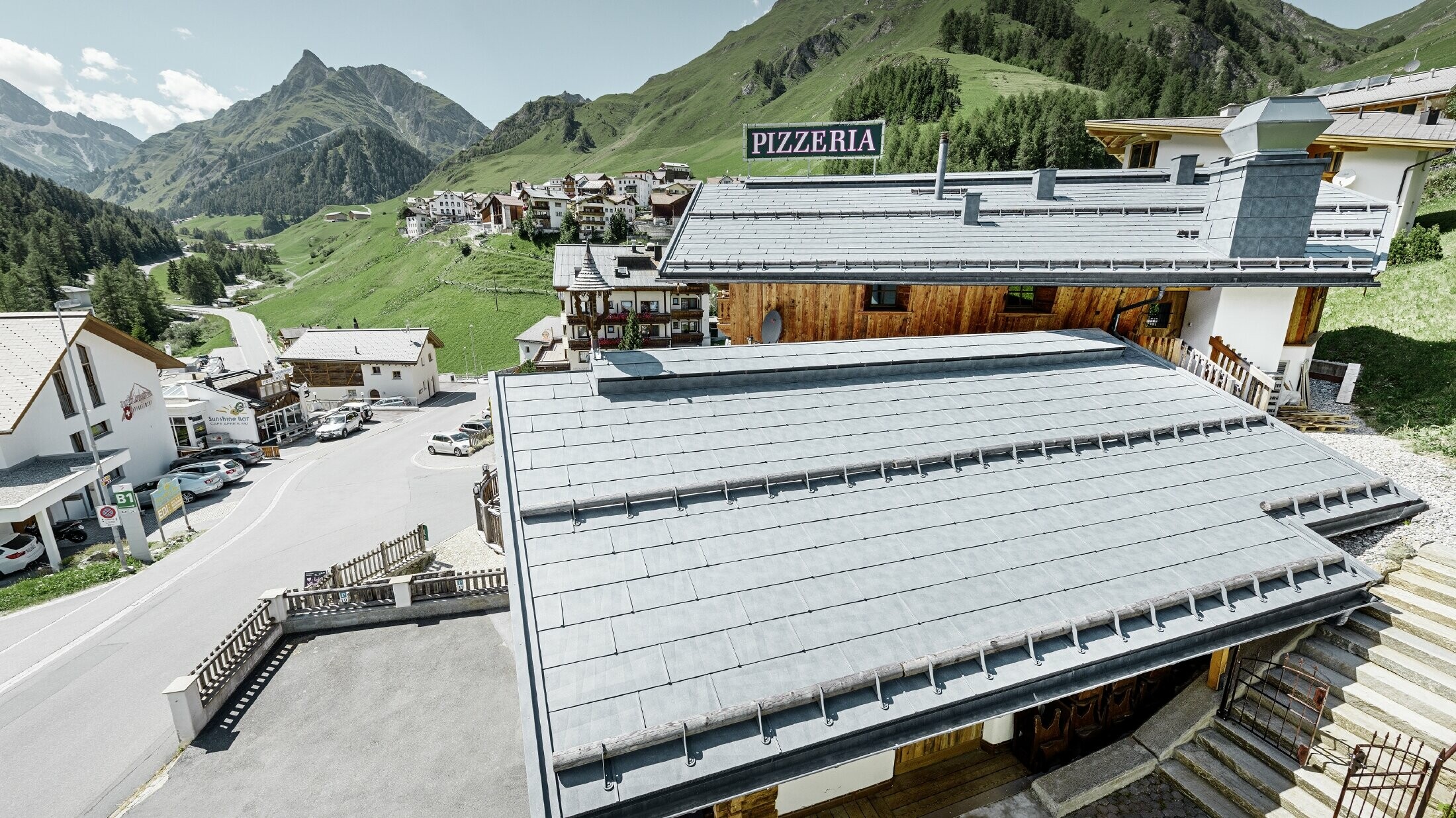 Restaurant Almrausch with a mountainous backdrop and a PREFA roof with FX.12 roof panels in stone grey and mountain snow guard brackets