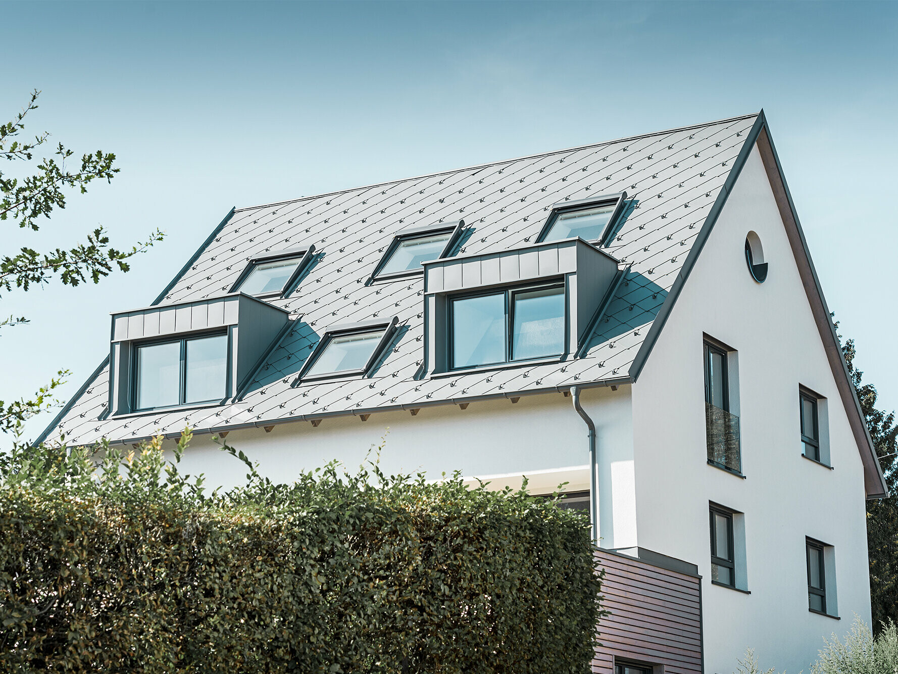 Roof refurbishment of a gabled roof with two dormers and four roof windows. The roof was covered with PREFA light grey 44 × 44 rhomboid roof tiles. The PREFA hanging gutter, also in light grey, was used for the guttering. 