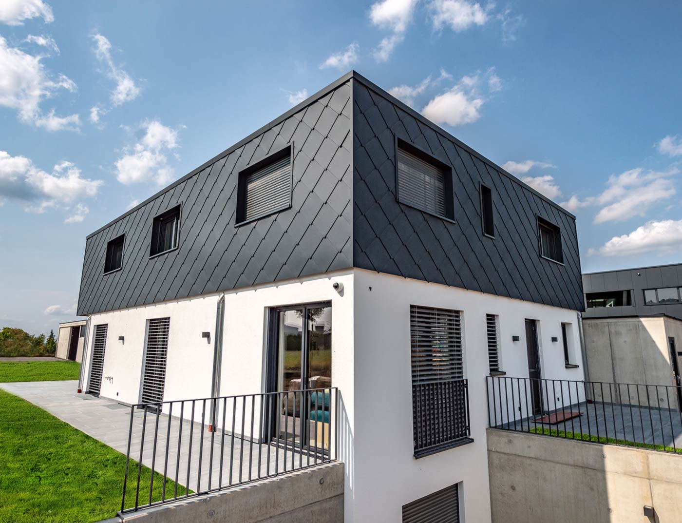 PREFA rhomboid wall tile 44 × 44 anthracite reference Modern new building with flat roof – the façade of the upper storey is clad with PREFA in anthracite 44 × 44 aluminium rhomboid wall tiles. The lower part of the façade is rendered in white.